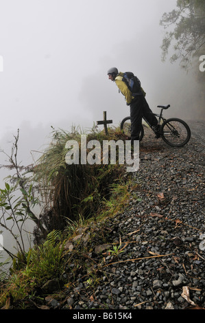 Gedenkstätte Kreuz vor einem Mountainbiker auf der Deathroad Blick besorgt über eine Böschung, Yungas, La Paz, Bolivien Stockfoto