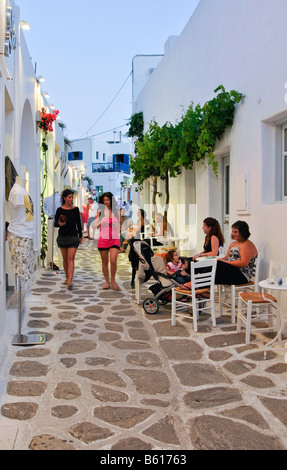 Zwei Frauen mit einem Kinderwagen sitzen in einer engen Gasse, wie Touristen, Naoussa, Paros, Kykladen, Griechenland, Europa vorbeikommen Stockfoto