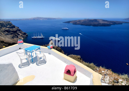 Terrasse eines kleinen Hotels vor dem blauen Meer, Segeln, Schiffe und die vulkanische Insel Nea Kameni, Thira, Fira, Santorini Stockfoto