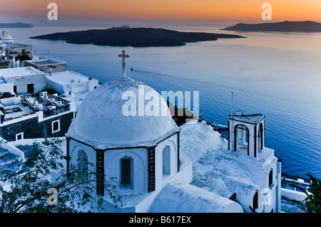 Weiße Kuppel-Kirche mit einem Kreuz bei Sonnenuntergang vor dem Meer und der vulkanischen Insel von Nea Kameni, Santorin, Kykladen, Griechenland Stockfoto