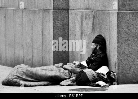 Ein schwarz-weiß Foto ein Obdachloser, ein Penner, ein Bettler, sitzen auf der Straße Ecke einer Straße in einer Großstadt. Stockfoto