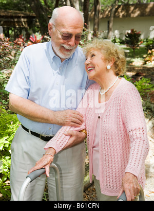 Behinderte ältere Frau schaut anbetend ihren Mann als er hilft ihr zu Fuß Stockfoto