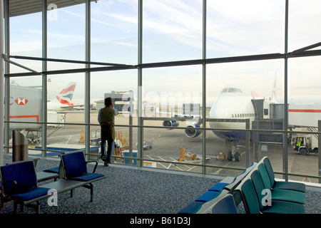 Ein Abflug-Lounge mit einem einsamen Passagier auf seinem Handy Blick auf Flugzeuge durch ein Fenster im Gespräch. Stockfoto