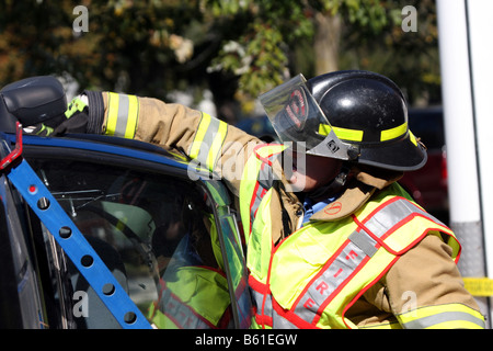 Die Fenster sind zerbrochen und die Feuerwehrmann ist Glas aus den Türrahmen eines stabilisierten rollovered Autos entfernen Stockfoto