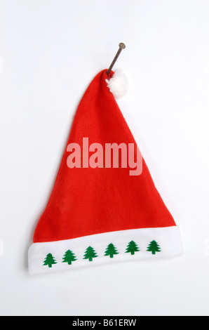 Rote Weihnachtsmütze mit weißem und grünem Design, die an einem Wandhaken zur festlichen Dekoration aufgehängt wird Stockfoto