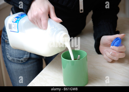 Milch in einen Becher gießen, während Sie zu Hause eine Tasse Tee mit heißem Getränk zubereiten Stockfoto