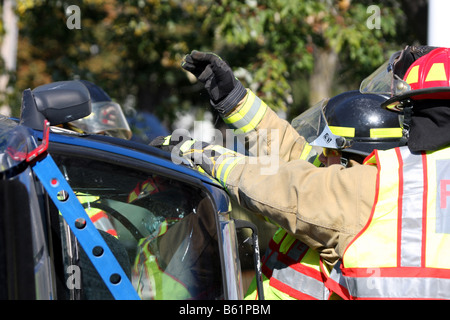 Die Fenster sind zerbrochen und die Feuerwehrmann ist Glas aus den Türrahmen eines stabilisierten rollovered Autos entfernen Stockfoto