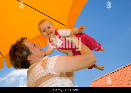 Mutter mit einem Baby, 10 Monate alt, spielen unter dem Sonnenschirm Stockfoto