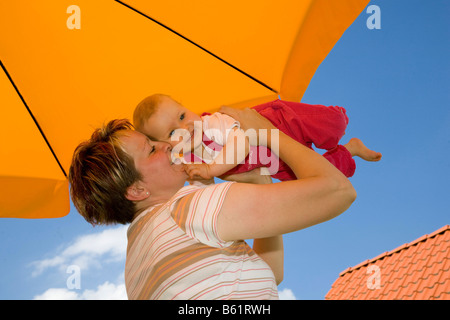 Mutter mit einem Baby, 10 Monate alt, spielen unter dem Sonnenschirm Stockfoto