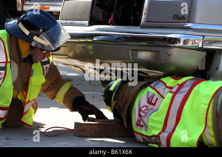 Zwei Feuerwehrleute Holzblöcke unter einem Fahrzeug nach einem Autounfall platzieren, um ihn zu stabilisieren, bevor Sie mit Bergung Stockfoto