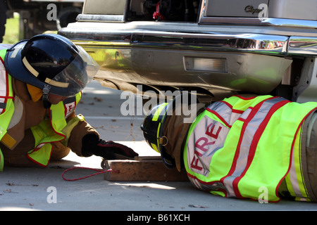 Zwei Feuerwehrleute Holzblöcke unter einem Fahrzeug nach einem Autounfall platzieren, um ihn zu stabilisieren, bevor Sie mit Bergung Stockfoto