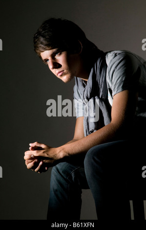 Junger Mann auf einem Stuhl sitzend in Gedanken versunken Stockfoto