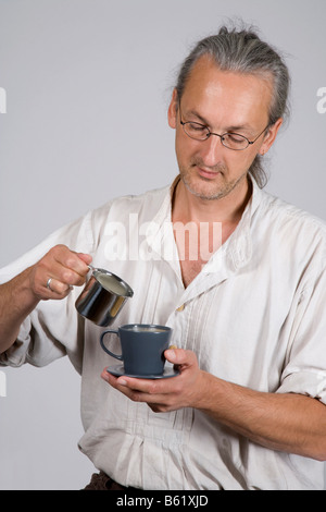 Man gießt Milch in eine Kaffeetasse Stockfoto