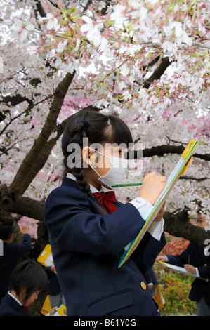 Schulmädchen in Uniform eine Elite Grundschule mit Gesichtsmaske auf einem Arbeitsblatt auf einem Klemmbrett in der botanischen arbeiten Stockfoto