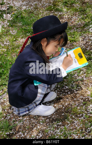 Schulmädchen in Uniform eine Elite Grundschule arbeiten auf einem Arbeitsblatt auf einem Klemmbrett im Botanischen Garten in K Stockfoto