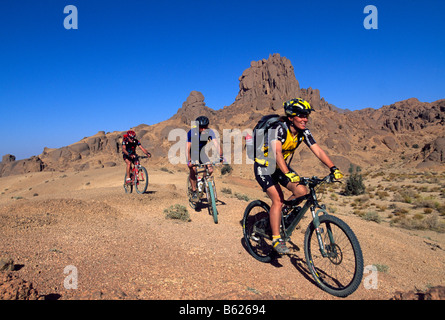 Mountainbiker, die auf einem Kamel reiten verfolgen, Ahaggar-Nationalpark, Ahaggar Berge, Algerien, Afrika Stockfoto
