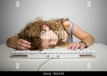 Junge Frau mit langen Haaren den Kopf auf eine Computer-Tastatur auf dem Tisch ruhen Stockfoto