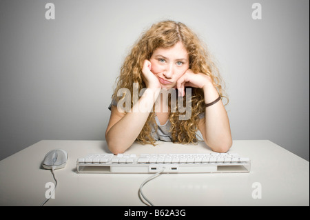 Junge Frau mit langen Haaren sitzen auf einem Tisch hinter einer Computertastatur frustriert Stockfoto