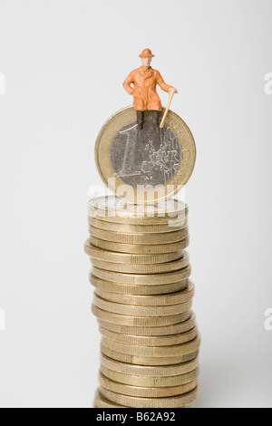 Rentner-Figur sitzt auf einem Stapel von Euro-Münzen, symbolisch für den Ruhestand Stockfoto