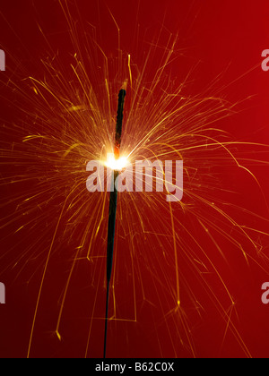 Brennende Wunderkerze vor rotem Hintergrund Stockfoto