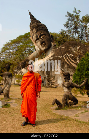 Buddhistischer Mönch trägt einen orangefarbenen Gewand vor einem liegenden Buddha Statue, Buddha Park, Suan Xieng Khuan, in der Nähe von Vientiane, Laos Stockfoto