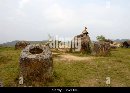 Eine Person sitzt auf einem geheimnisvollen Bellarmines, Plain of Jars, Ort der Entdeckung Nr. 1 (Thong Hai Hin), Xieng Khuang Pr Stockfoto