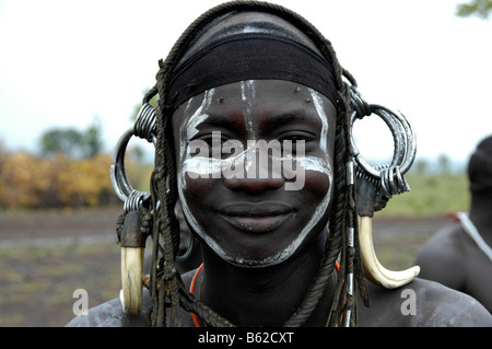 Porträt eines lächelnden jungen Mannes vom Stamm Mursi, machte wild, schweren Kopfschmuck der Zähne von einem Eber in der Nähe von Jinka, Äthiopien, Stockfoto