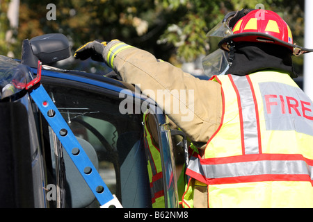 Die Fenster sind zerbrochen und die Feuerwehrmann ist Glas aus den Türrahmen eines stabilisierten rollovered Autos entfernen Stockfoto