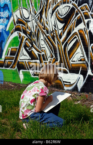 Mädchen zeichnen oder Kopieren von Graffiti-Kunst auf einer gemauerten Wand Spray lackiert als Bestandteil ein Community-Projekt zu einen lokalen Park erhellen Stockfoto