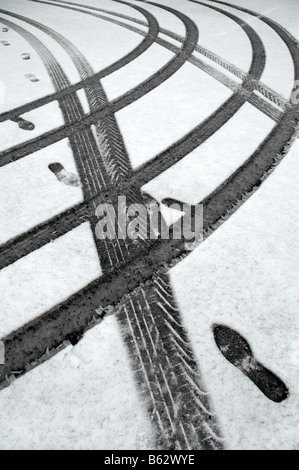 Auto-Reifenspuren und Fußabdrücke in flachen Schnee. Stockfoto