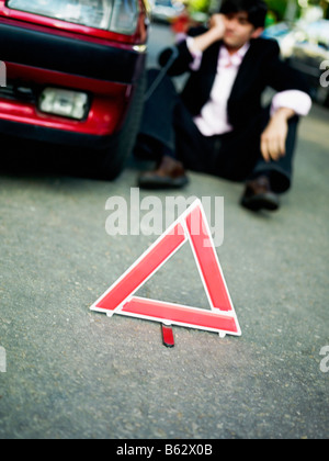 Mitte erwachsenen Mannes durch eine kaputte Auto hinter einem Warndreieck auf der Straße sitzen Stockfoto