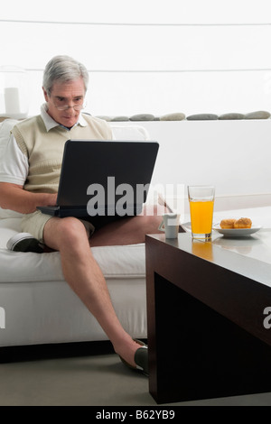 Ältere Mann arbeitet auf einem Laptop mit Frühstück auf dem Tisch Stockfoto