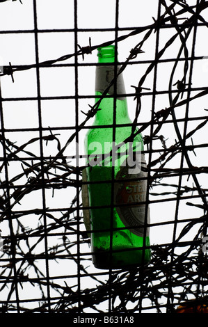 Leere Bierflasche auf Metallrost umgeben von Stacheldraht Stockfoto