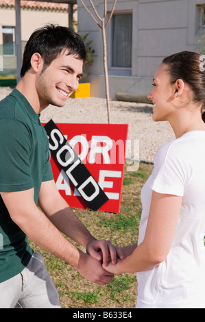 Junges Paar Hand in Hand der jeweils anderen vor eine verkaufte Informationstafel Stockfoto