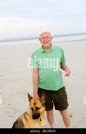 Porträt eines älteren Mannes steht mit seinem Hund am Strand Stockfoto