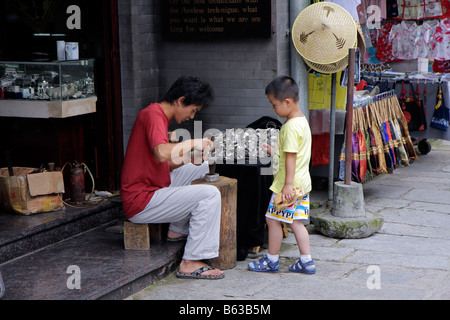 Chinesischer Mann und junge, die Herstellung von Schmuck vor seinem Strassenlokal, Yangshuo, China Stockfoto