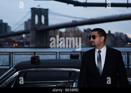 Ein Detektiv mit Sonnenbrille stützt sich auf ein Cougar 1967 unter der Brooklyn Bridge mit einer Sirene Licht auf dem Dach. Stockfoto