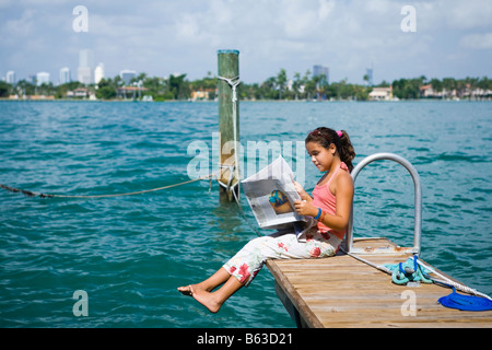 Seitenansicht eines Mädchens auf dem Steg sitzen und eine Zeitung lesen Stockfoto