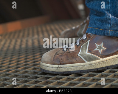 Füße in Converse Sneakers, stehend auf einem Eisen-Grill. Stockfoto