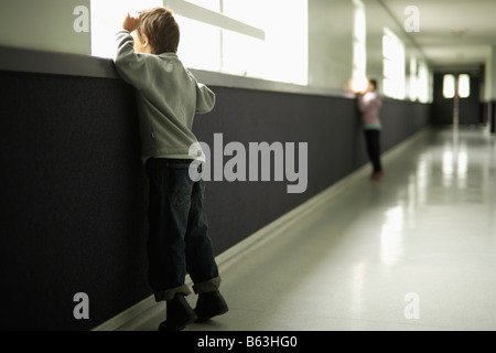 Jungen im Alter von sechs Mädchen im Alter von fünf Stand in der Schule Flur Blick aus Fenster Stockfoto