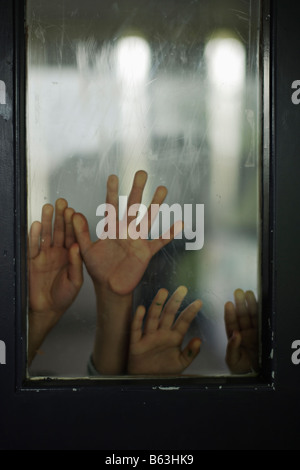 Händen der fünf Jahre altes Mädchen und sechs Jahre alten Jungen gegen die Glasscheibe in der Tür Stockfoto