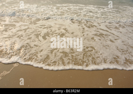 Der weiße Schaum, der sanft brechenden Wellen macht eine Wellenlinie an einem Sandstrand Stockfoto
