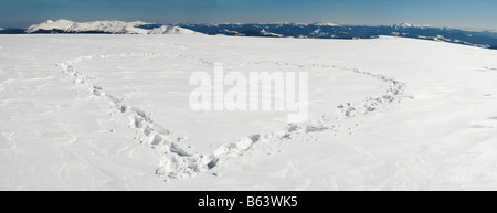 Menschlichen Fußabdruck bilden die Herzform auf Schnee bedeckten Berg-Plateau und Bergketten hinter. Fünf Schüsse feststeppen Bild. Stockfoto
