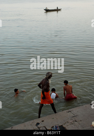 Heiliger Mann zu Fuß durch den Fluss Ganges und Jungs spielen im Wasser. Varanasi. Indien. Stockfoto