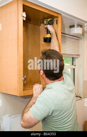 Carpenter einschrauben massivem Ahorn Schränke in die weiße Wand vor Ort in Bohrer ist Farbe tropft nicht logo Stockfoto