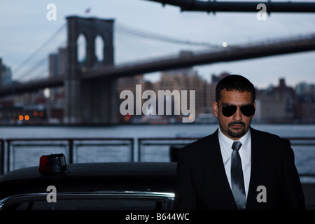 Ein Detektiv mit Sonnenbrille stützt sich auf ein Cougar 1967 unter der Brooklyn Bridge mit einer Sirene Licht auf dem Dach. Stockfoto
