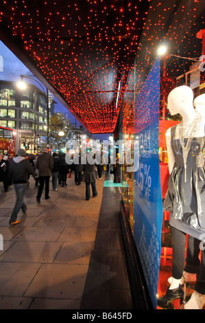 Christmas Lights & Reflexionen in den Kaufhäuser Fenster Anzeige Weihnachtsgeschenk Idee Käufer zu Fuß von der Oxford Street Pflaster London England Großbritannien Stockfoto