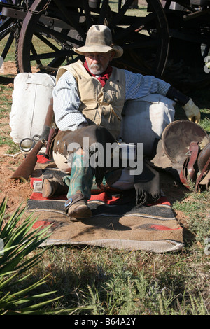 Ein Oldtimer Cowboy lehnte sich gegen seinen Pack und Sattel neben Chuck Wagon Stockfoto