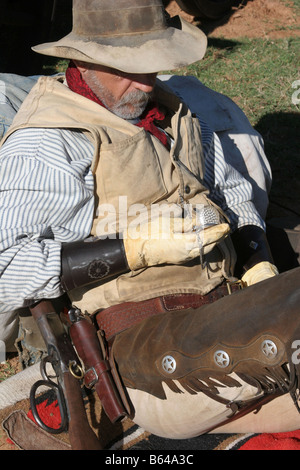 Ein Oldtimer Cowboy lehnte sich gegen seinen Pack und Sattel neben den Planwagen überprüft seine Taschenuhr Stockfoto