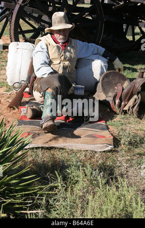 Ein Oldtimer Cowboy lehnte sich gegen seinen Pack und Sattel neben Chuck Wagon Stockfoto